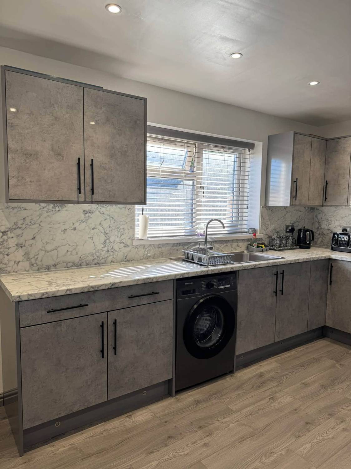 Grey concrete-effect L-shaped kitchen with marble-effect worktop and splashback